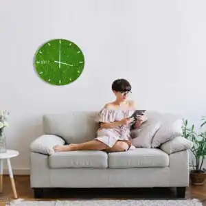 žena sediaca na gauči s knihou a hodinami na stene za ňou machovy obraz, stabilizovany mach, machová stena, machová dekorácia