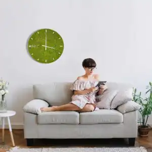 žena sediaca na gauči s tabletom v ruke a hodinami na stene za sebou machovy obraz, stabilizovany mach, machová stena, machová dekorácia