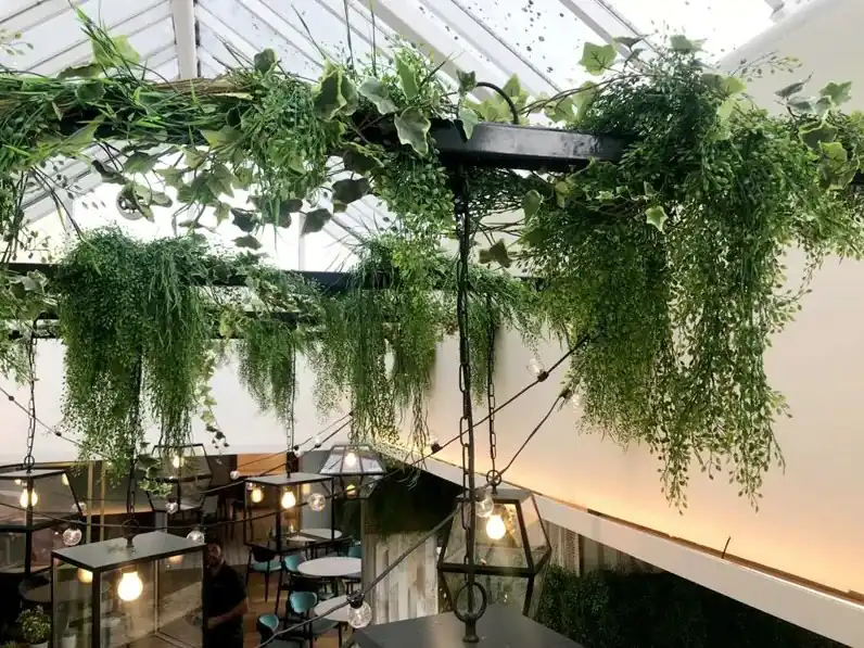 Visiace umelé zelené rastliny pod moderným preskleným stropom